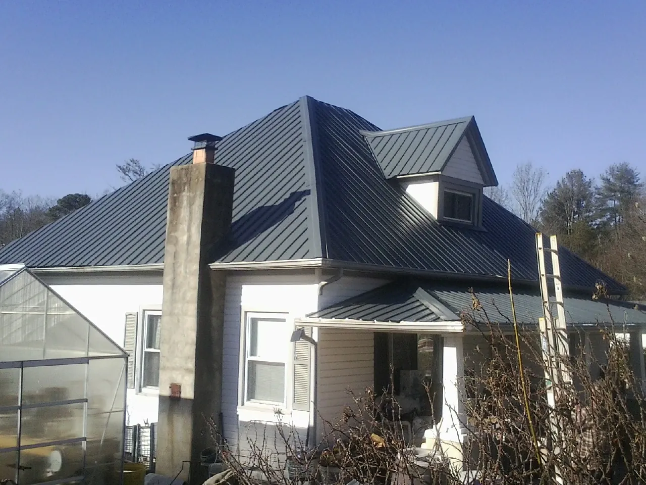Dark blue standing seam metal roof on a white farmhouse with dormer — Slate & Tile Roof Repair by Roofing Brothers in Stanley