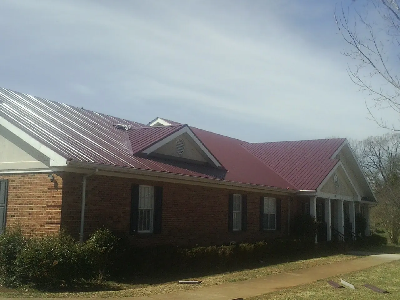 Red metal roof with gabled entries on a long brick building, from a Hail Damage Roof Repair job in Stanley